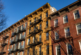 Looking up at a row of colorful old brick residential buildings with fire escapes along a street in Williamsburg Brooklyn of New York City