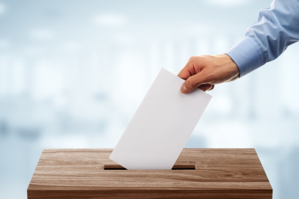 A disembodied hand puts a ballot in a voting box.